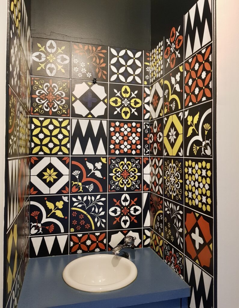 Carrelage Azulejos Salle de Bain : Déco Vintage et Colorée Petit lavabo sur plan bleu devant un mur de carrelage azulejos coloré aux motifs géométriques et floraux vintage.
