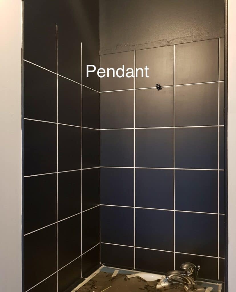 Douche en carrelage noir à joints blancs avec texte 'Pendant' indiquant l'emplacement d'un futur luminaire suspendu.