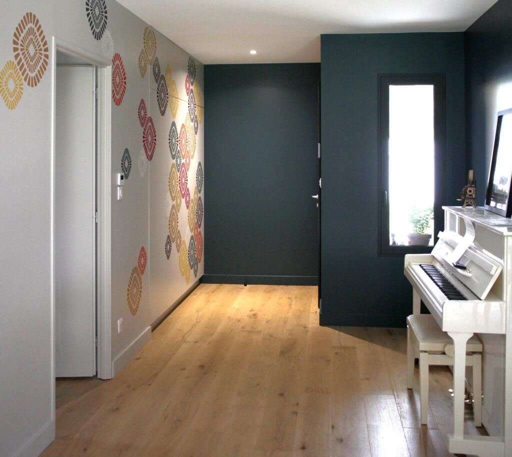 Décoration murale géométrique, couloir parquet bois clair, mur bleu canard et piano droit blanc.