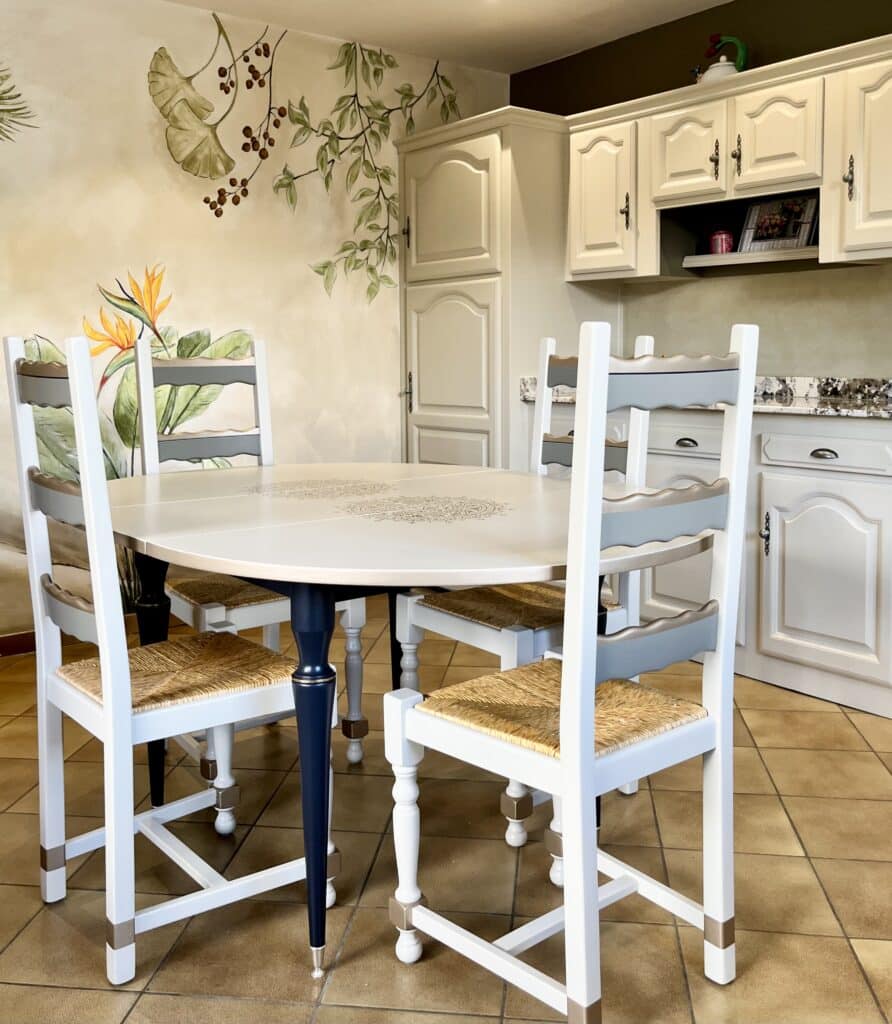 Salle à manger style campagne chic avec fresque murale Coin repas avec table blanche, chaises en bois peintes et fresque murale de fleurs et feuilles de ginkgo.