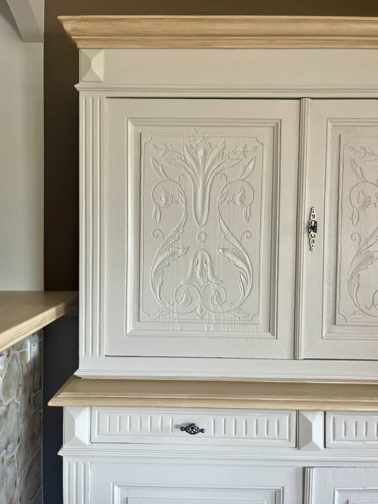 Buffet sculpté blanc cassé avec détails floraux et étagère en bois clair.