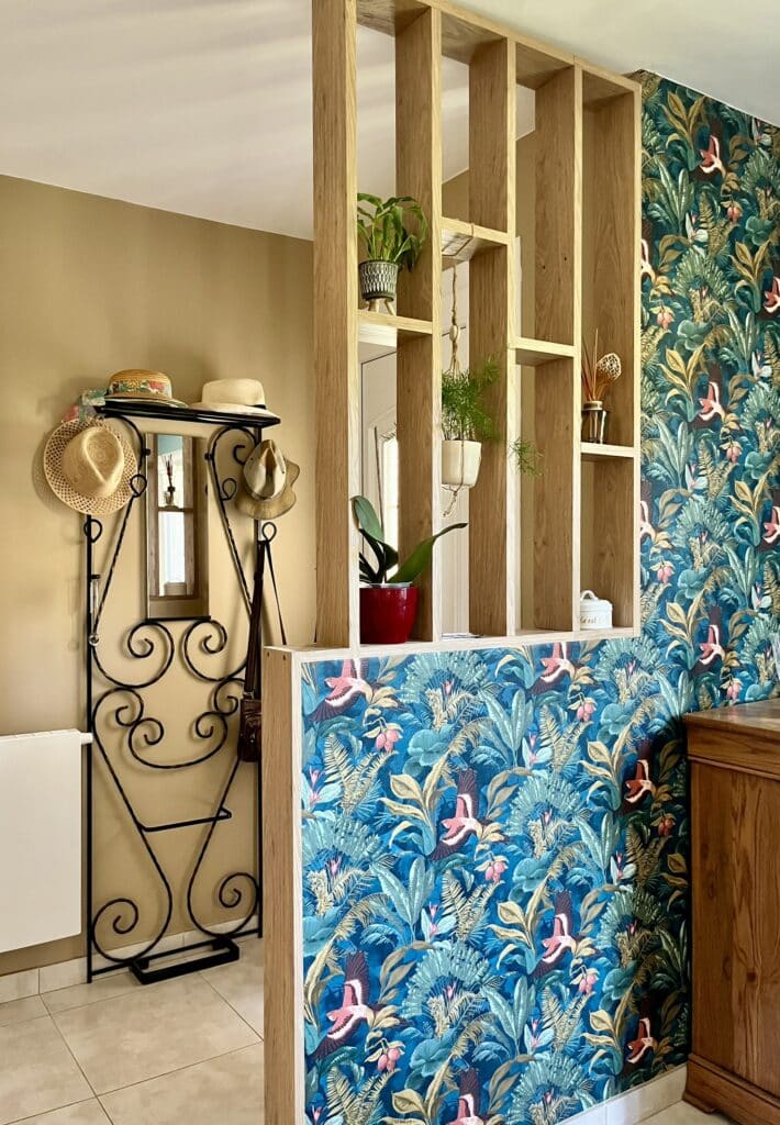 Séparation de pièce en bois avec papier peint tropical bleu et étagères fleuries à côté d'un porte-manteau vintage.