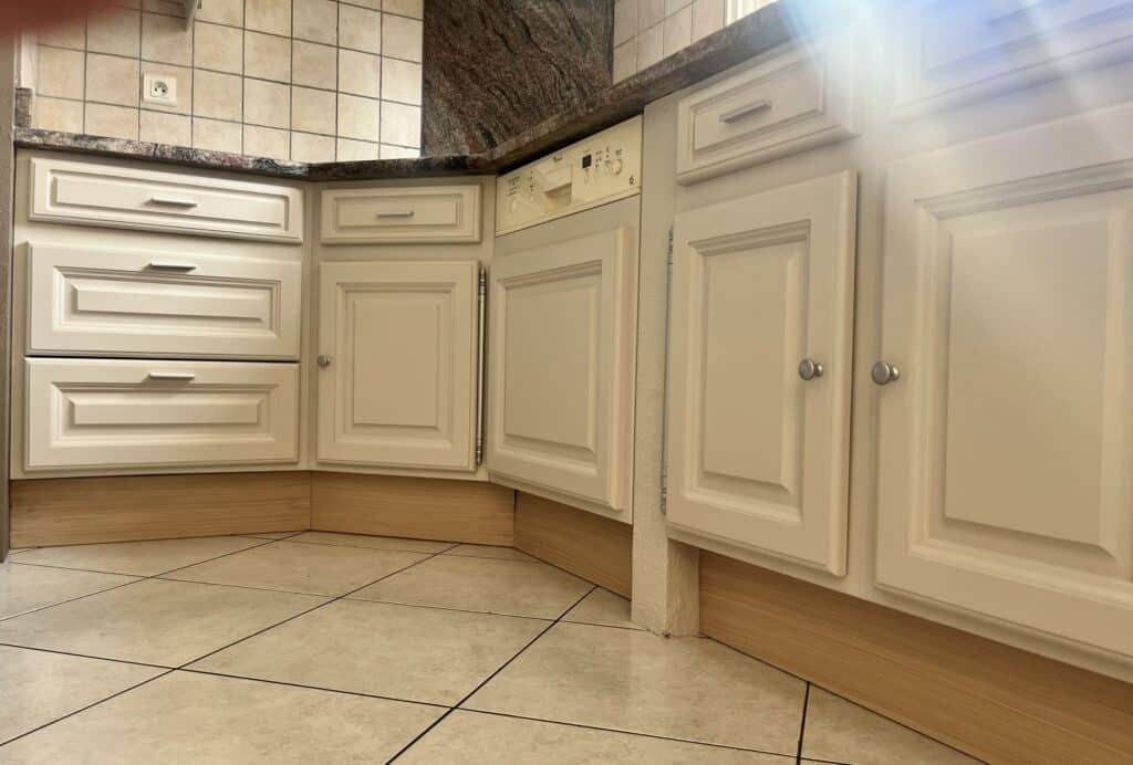 Placards de cuisine crème, plan de travail en granit, carrelage beige et lave-vaisselle encastré.