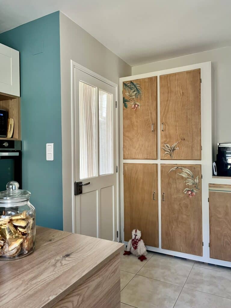 Déco de Cuisine : Placard en Bois Peint et Mur Bleu Canard Cuisine moderne avec mur bleu canard, porte blanche et placard en bois décoré de motifs floraux.