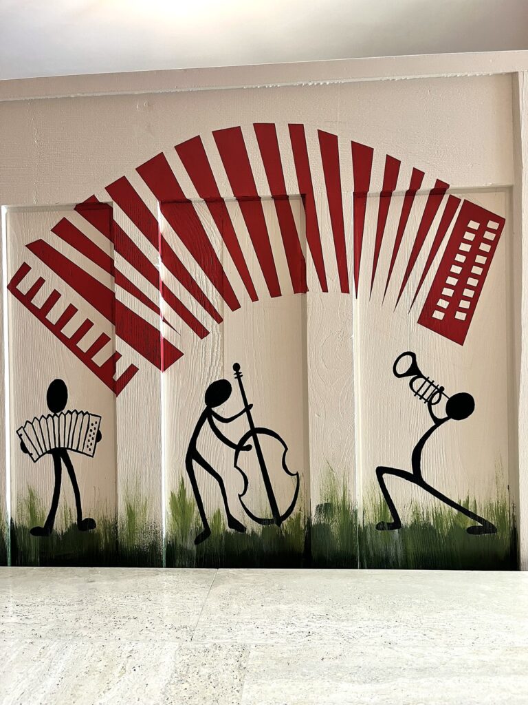 Mural de musiciens stylisés jouant accordéon, contrebasse et trompette sous un grand soufflet d'accordéon rouge.