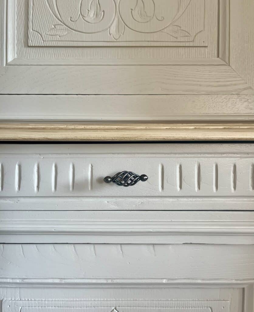 Détail de meuble en bois blanc sculpté avec bouton de tiroir en fer forgé noir torsadé.