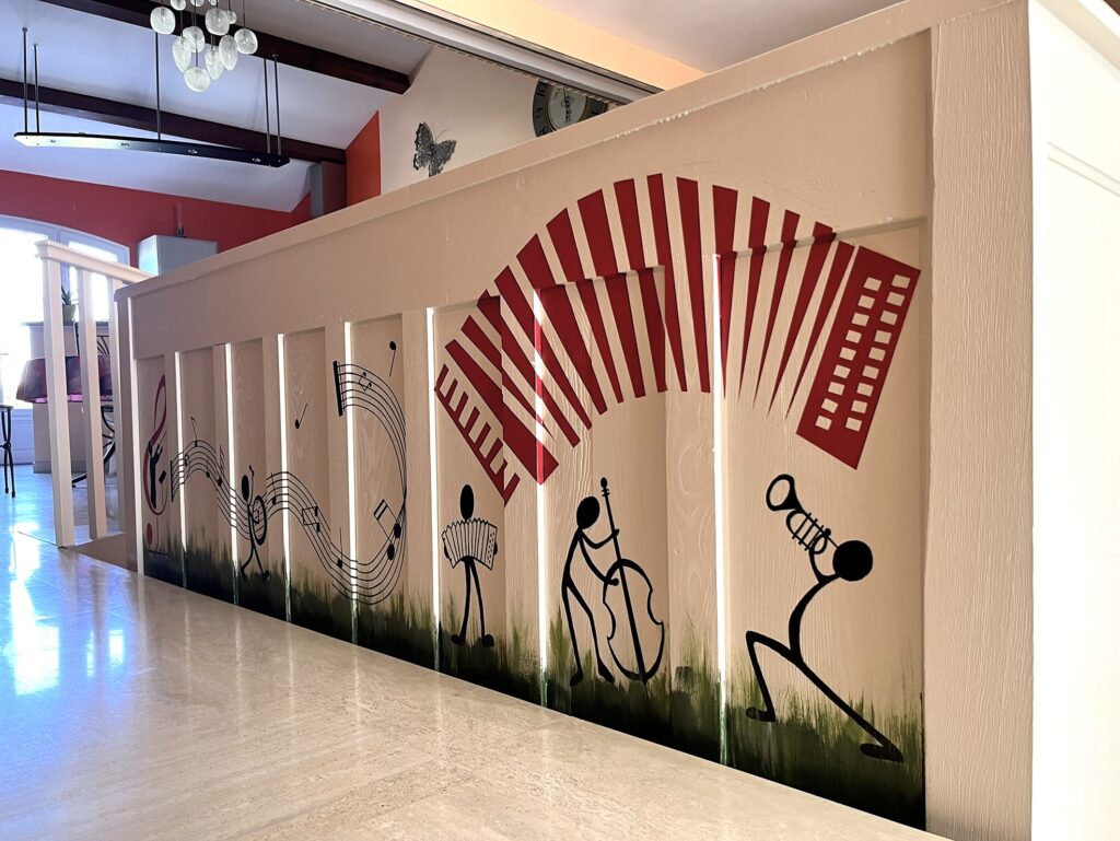 Décoration Murale Musique : Fresque Silhouette et Accordéon Peinture murale de musiciens stickman et accordéon rouge sur une rampe intérieure blanche.