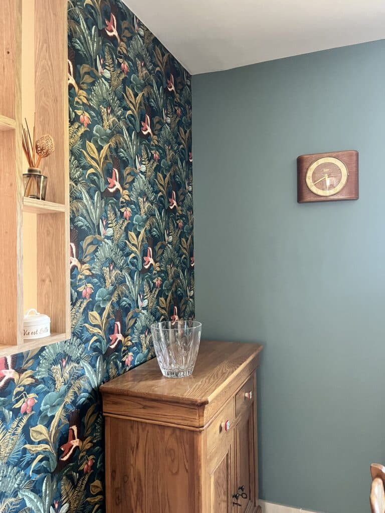 Papier peint jungle, mur bleu canard, buffet en bois et pot 'Vie est Belle' pour une décoration vintage.