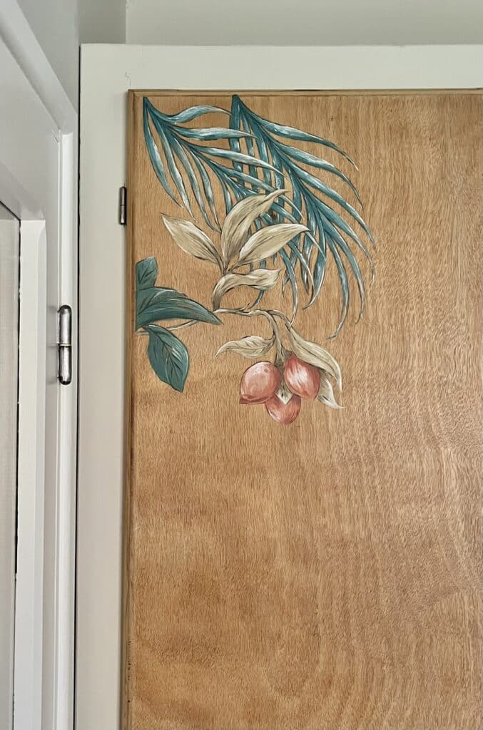 Peinture botanique de feuilles tropicales bleues et fruits rouges sur une porte en bois naturel.