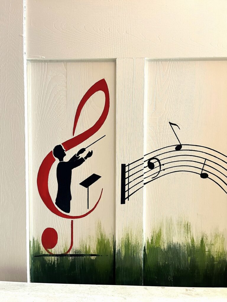 Chef d'orchestre en silhouette dans une clé de sol rouge avec portée musicale sur bois.