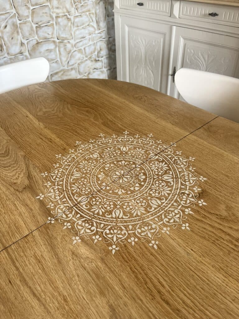 Table en bois avec mandala blanc au pochoir, mur en pierre et buffet blanc.