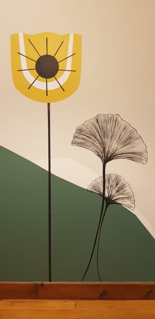 Art mural minimaliste : fleur jaune stylisée et feuilles de ginkgo noires sur fond géométrique beige et vert.