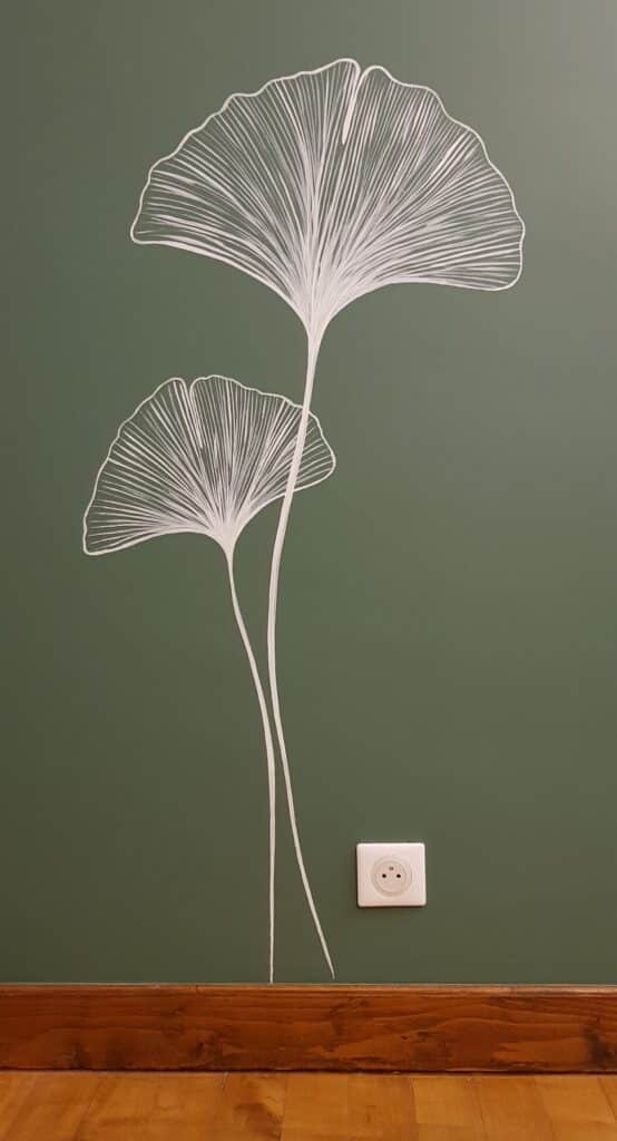 Fresque de feuilles de ginkgo blanches sur mur vert olive au-dessus d'une plinthe en bois.