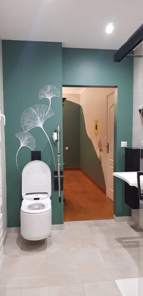 WC suspendu blanc, mur vert avec motif ginkgo et barre d'appui PMR.